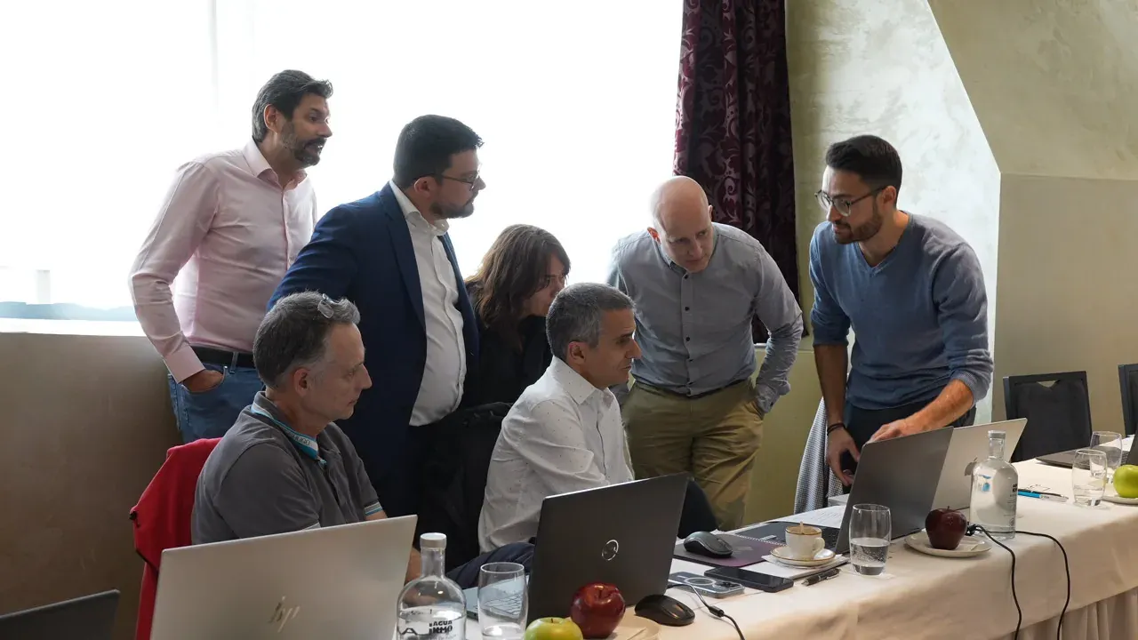 Several attendees standing behind two seated colleagues, everyone looking at the same screen