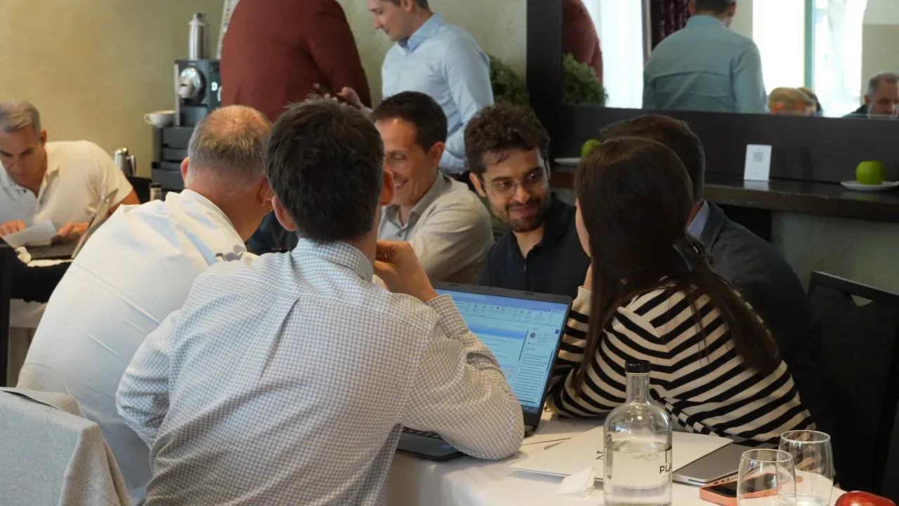 Six people around a long table, each with their laptop open on a different screen